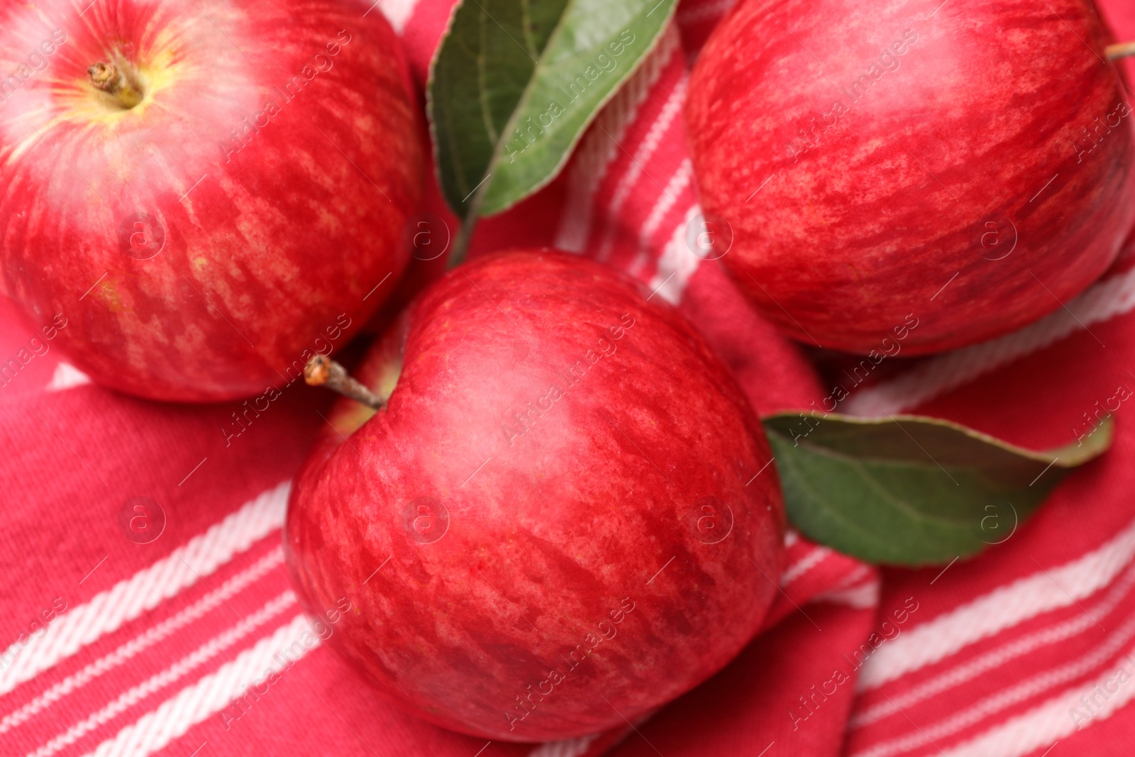 Photo of Fresh red apples with leaves on red cloth, flat lay