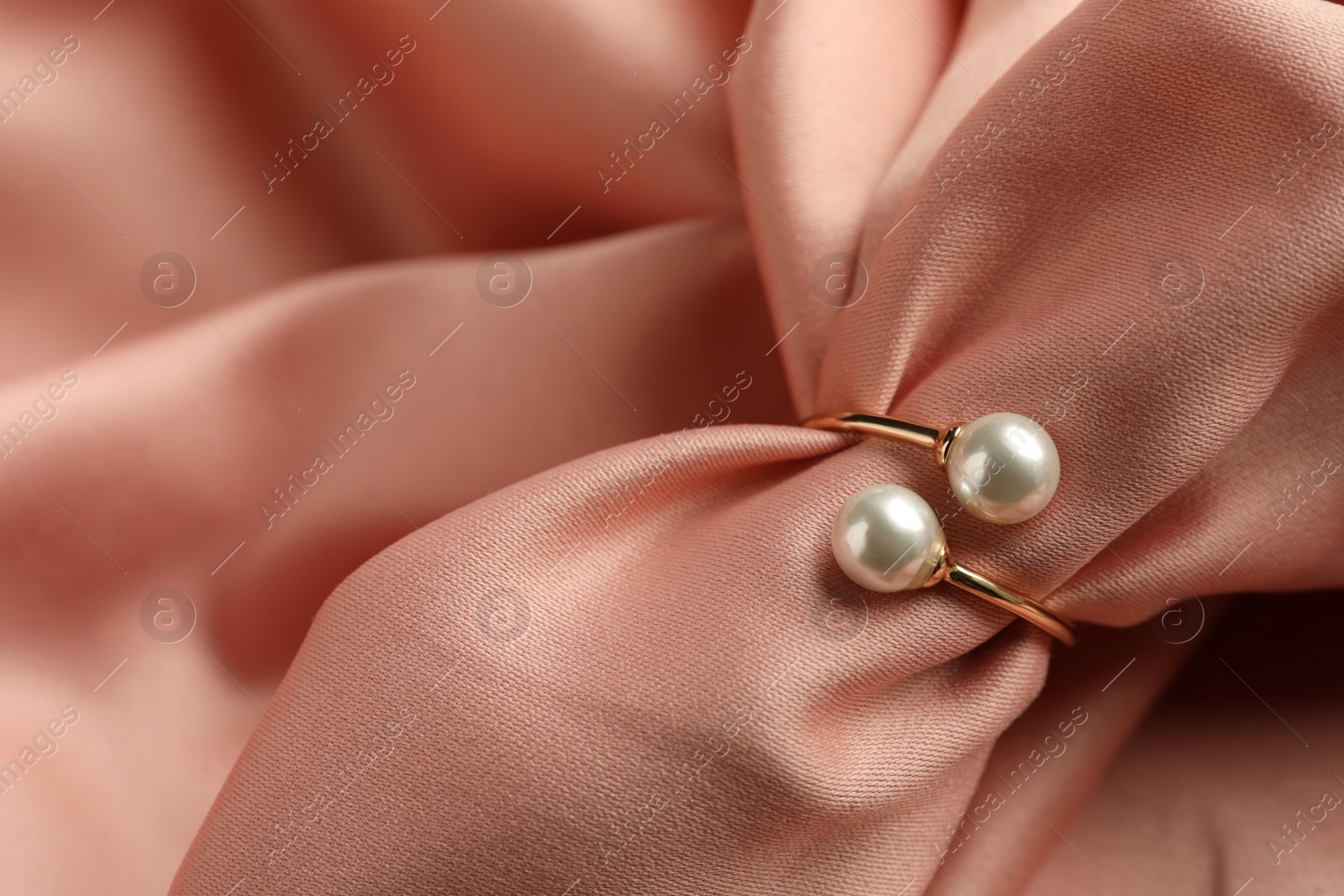 Photo of Elegant golden ring with pearls on pink silk, closeup