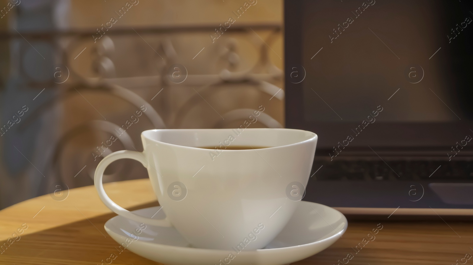 Photo of Cup of aromatic coffee and laptop on wooden table outdoors, closeup