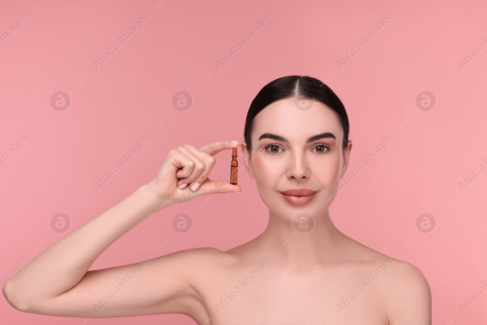 Photo of Beautiful young woman holding skincare ampoule on pink background