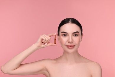 Beautiful young woman holding skincare ampoule on pink background