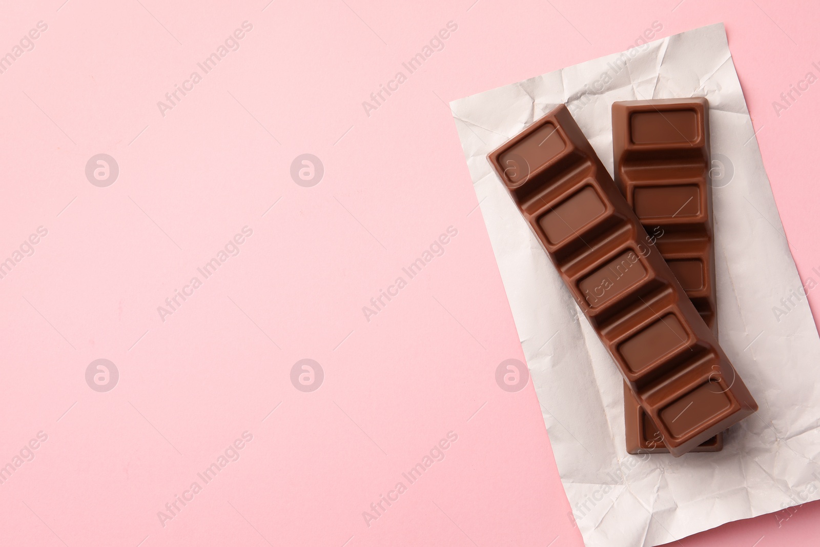 Photo of Paper wrap with delicious chocolate bars on pink background, top view. Space for text