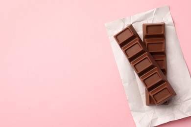 Paper wrap with delicious chocolate bars on pink background, top view. Space for text