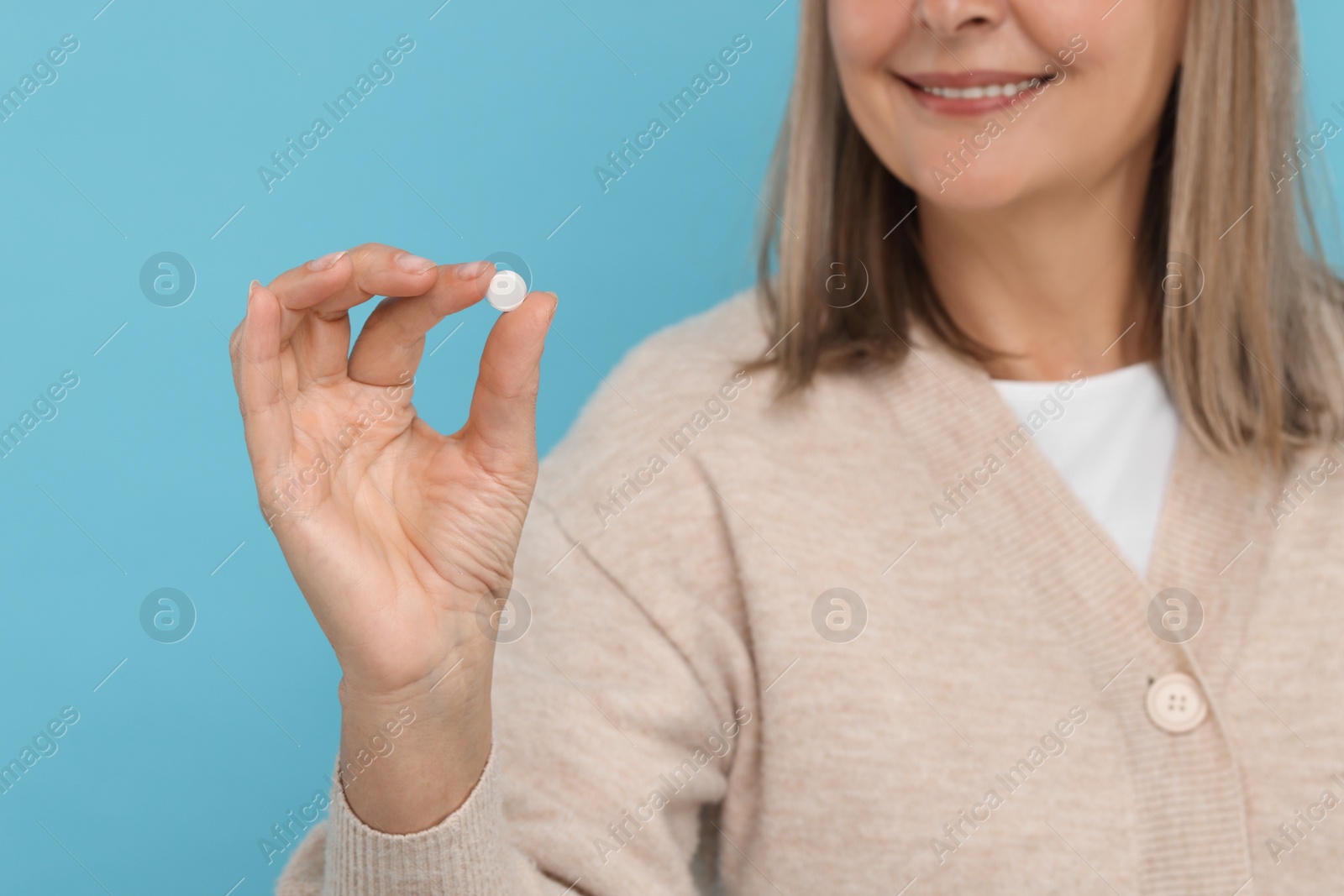 Photo of Senior woman with pill on light blue background, closeup