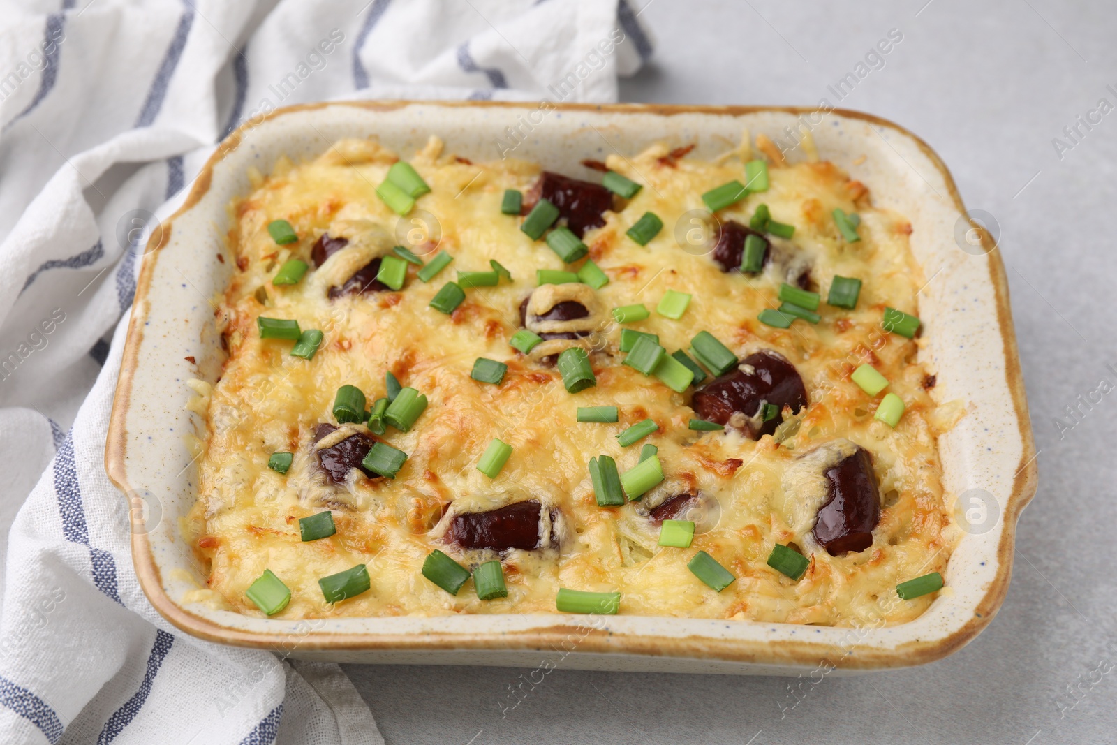 Photo of Tasty sausage casserole with green onions in baking dish served on white table, closeup