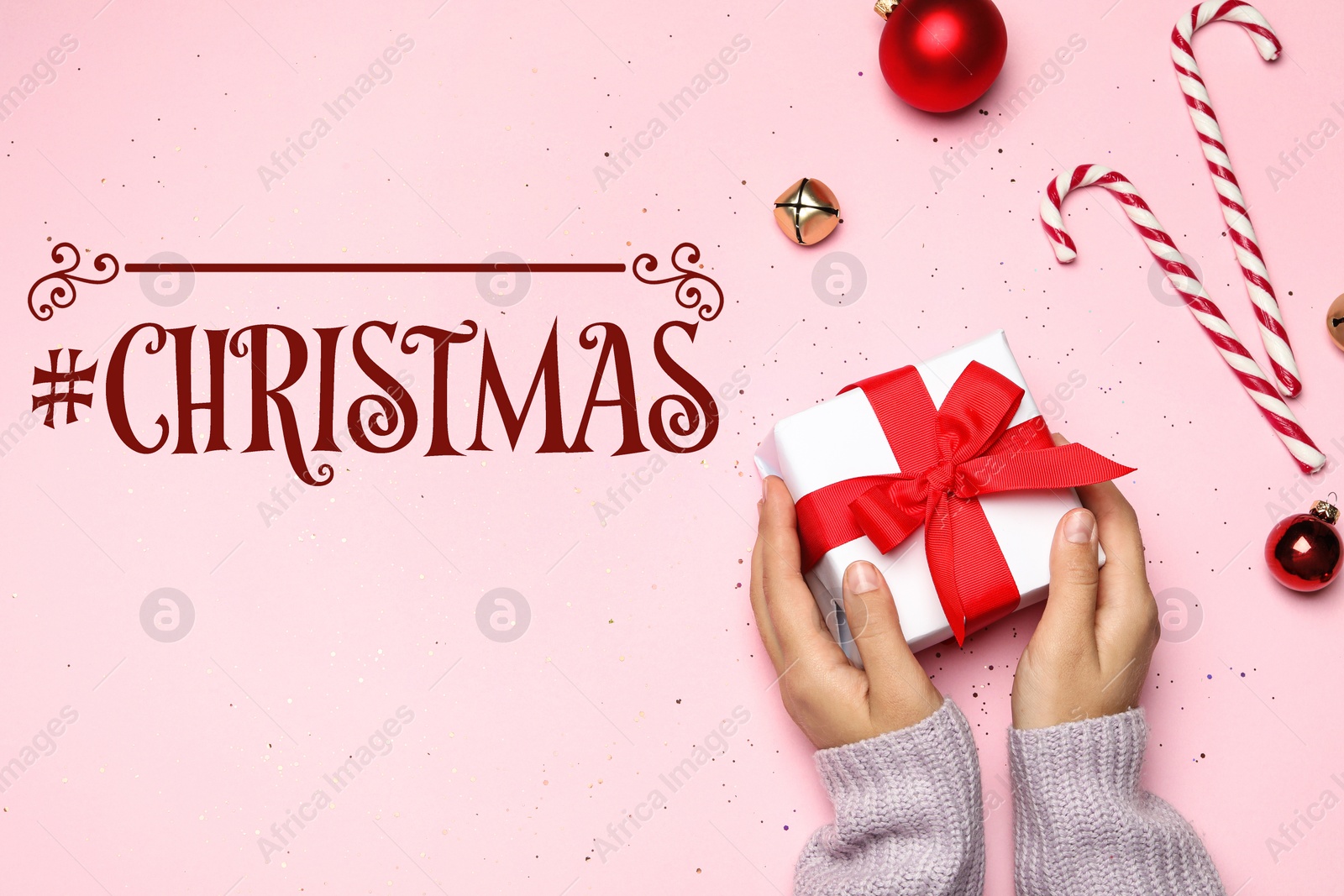 Image of Young woman holding Christmas gift near hashtag Christmas on pink background, flat lay