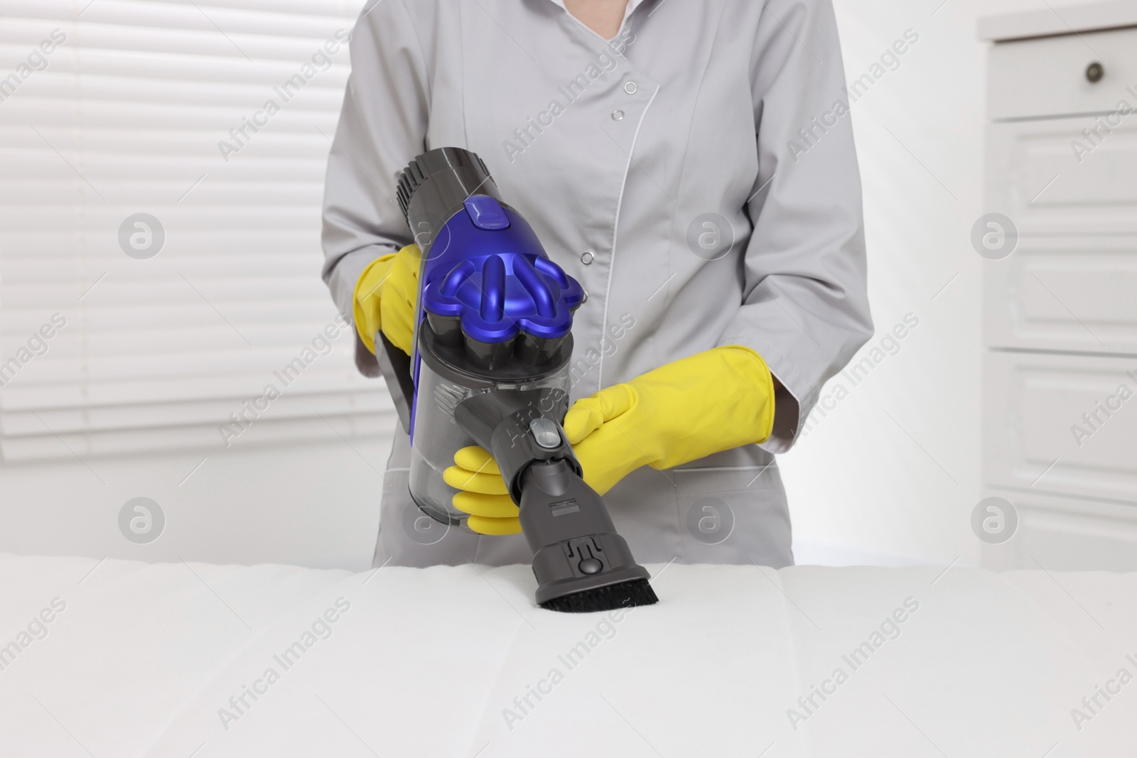 Photo of Woman in gloves disinfecting mattress with vacuum cleaner indoors, closeup