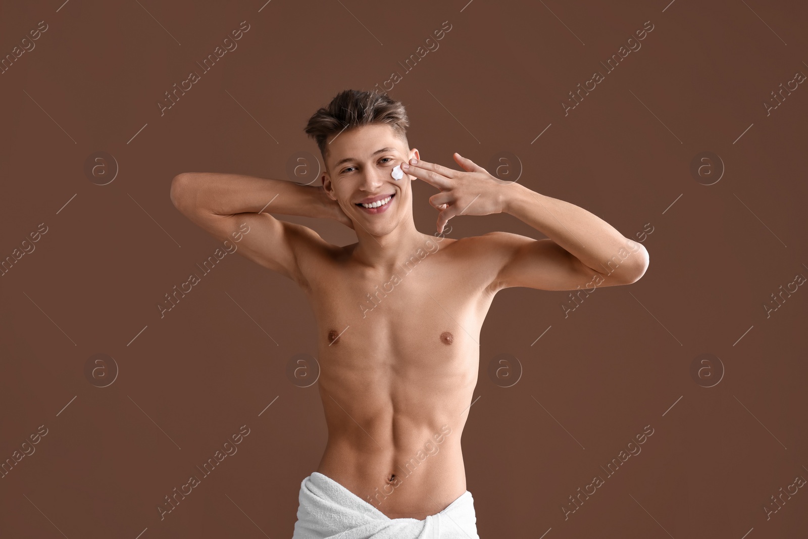 Photo of Handsome man applying moisturizing cream onto his face on brown background