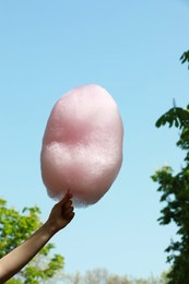 Woman holding sweet cotton candy against blue sky, closeup