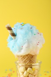 Photo of Sweet cotton candy in waffle cone on yellow background, closeup