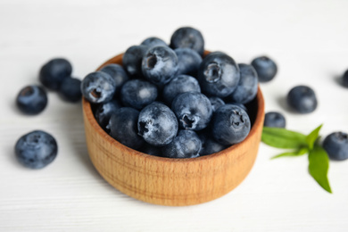 Fresh ripe blueberries in bowl on white wooden table, closeup