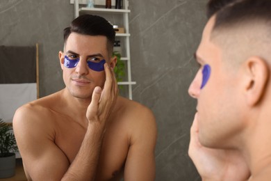 Photo of Man applying blue under eye patches near mirror at home