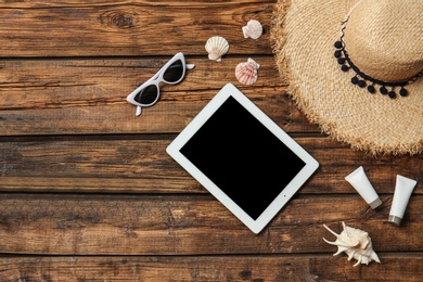 Flat lay composition with tablet and beach objects on wooden background