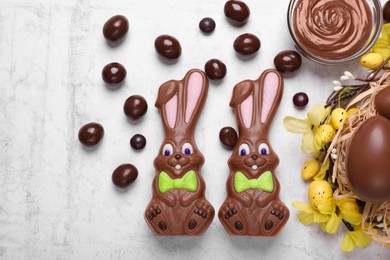 Flat lay composition with chocolate Easter bunnies, eggs and candies on white textured table