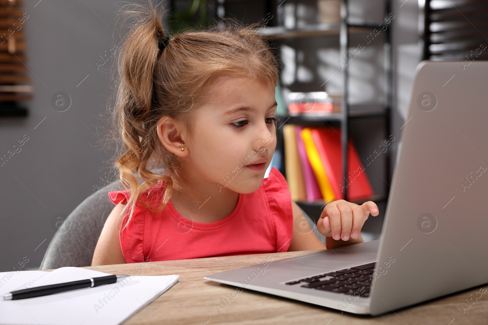 Photo of Cute little girl doing homework with laptop at table