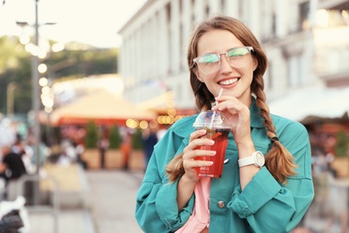 Photo of Young woman with refreshing drink on city street. Space for text