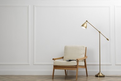 Stylish room interior with lamp and armchair near white wall. Space for text
