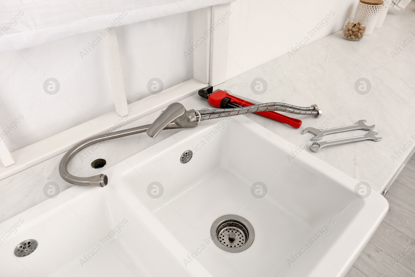 Photo of Plumber's tools and water tap ready for installation near sink on countertop in kitchen