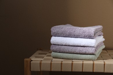 Photo of Stacked terry towels on wicker bench near beige wall, space for text