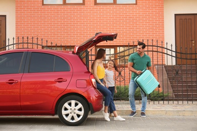 Photo of Happy family with suitcase near their car on street
