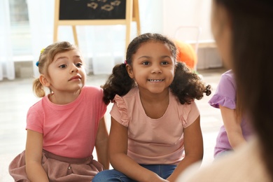 Photo of Cute little children listening to teacher indoors. Kindergarten playtime activities
