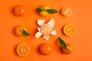 Delicious tangerines and green leaves on orange background, flat lay