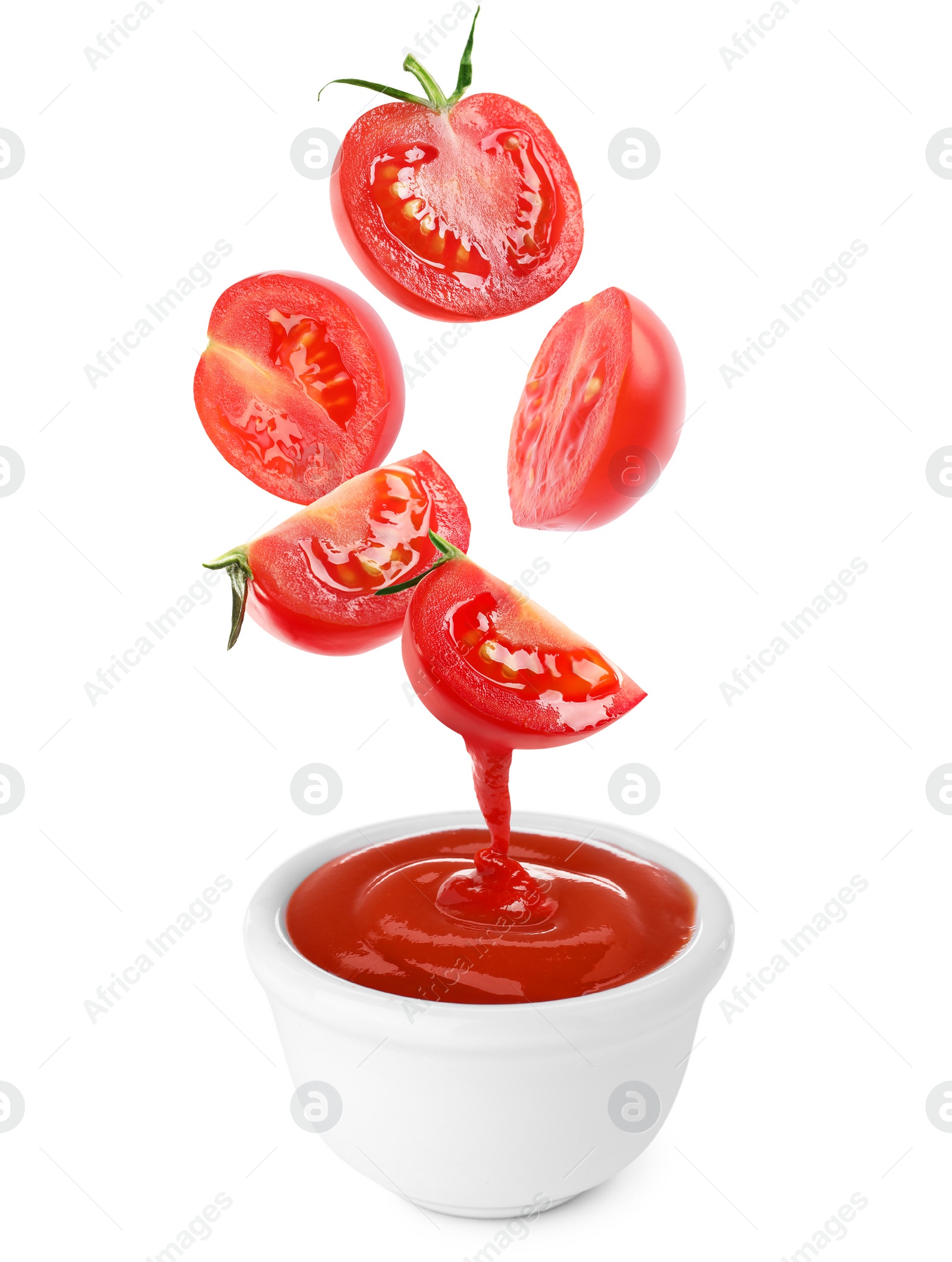 Image of Cut tomatoes falling into bowl with organic ketchup on white background