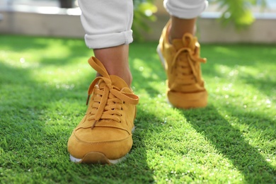 Photo of Young woman wearing stylish sneakers on green grass, closeup