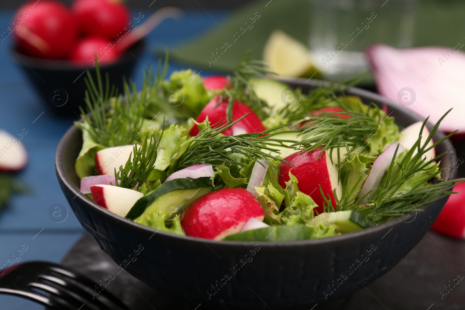 Photo of Tasty salad with radish in bowl on blue table, closeup