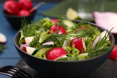 Tasty salad with radish in bowl on blue table, closeup