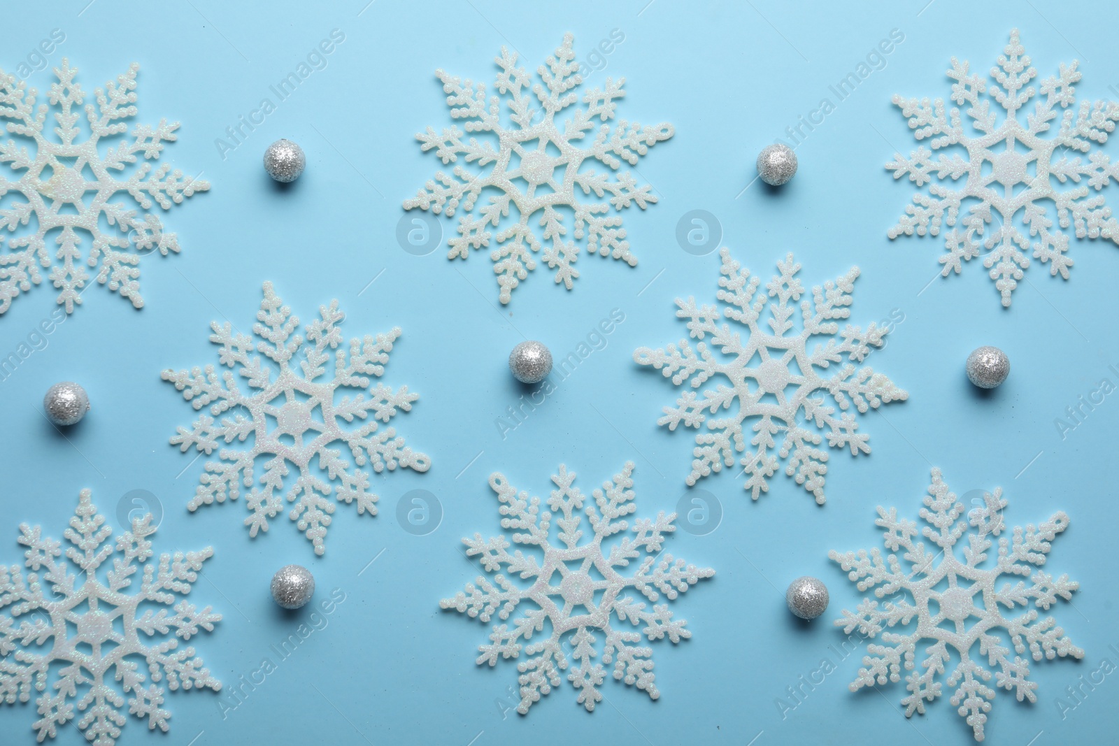 Photo of Beautiful snowflakes and decorative balls on light blue background, flat lay