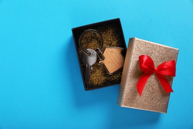 Photo of Key with trinket in shape of house and gift box on light blue background, flat lay. Space for text. Housewarming party