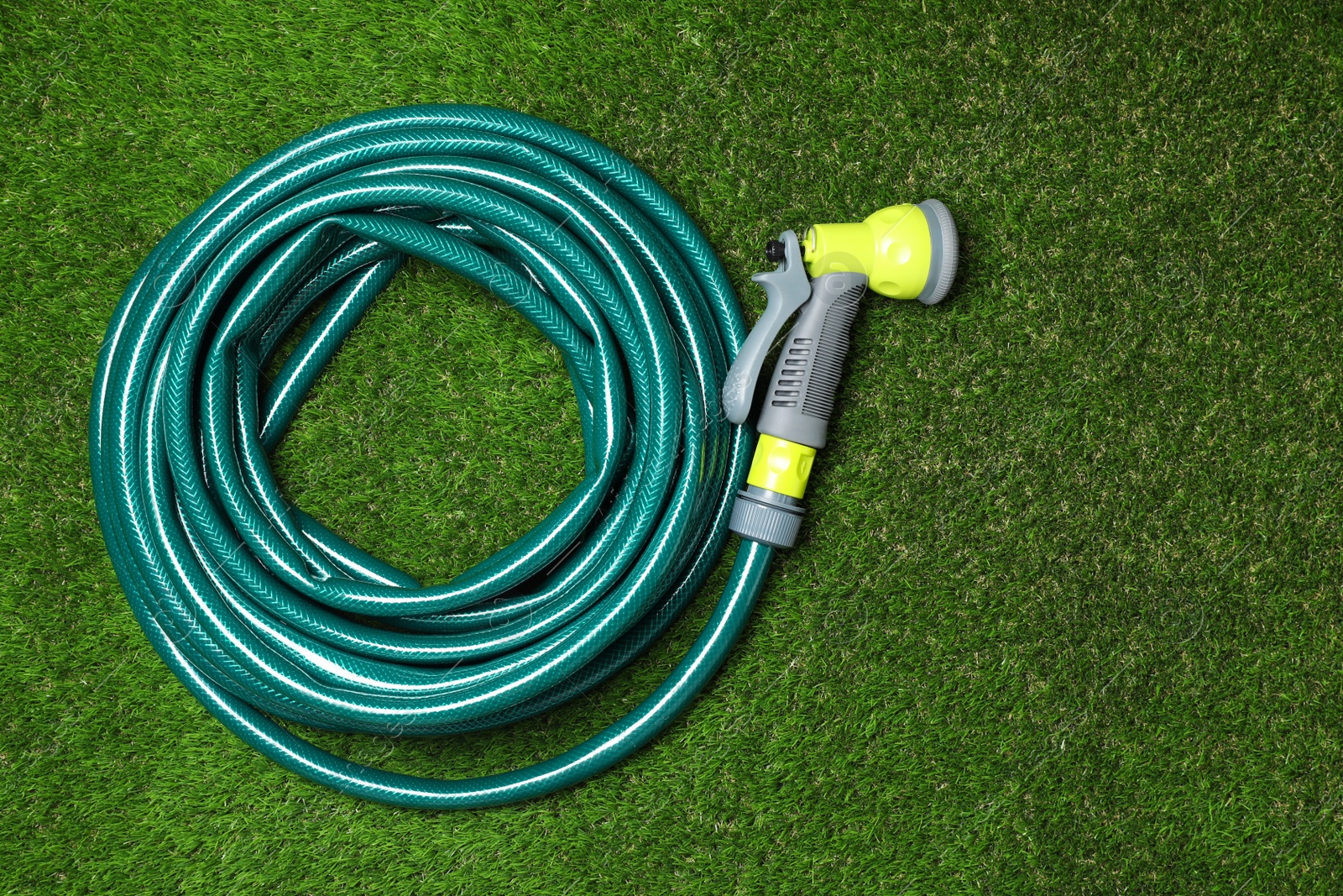 Photo of Watering hose with sprinkler on green grass, top view