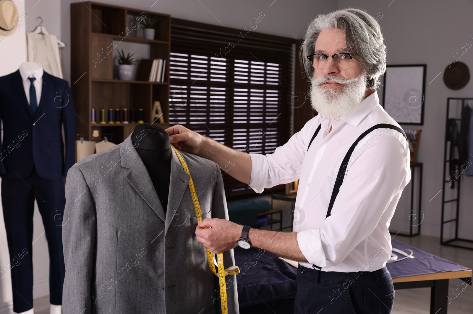 Photo of Professional tailor with measuring tape working in atelier