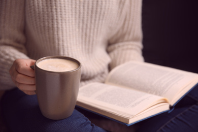 Photo of Woman with cup of coffee reading book at home, closeup