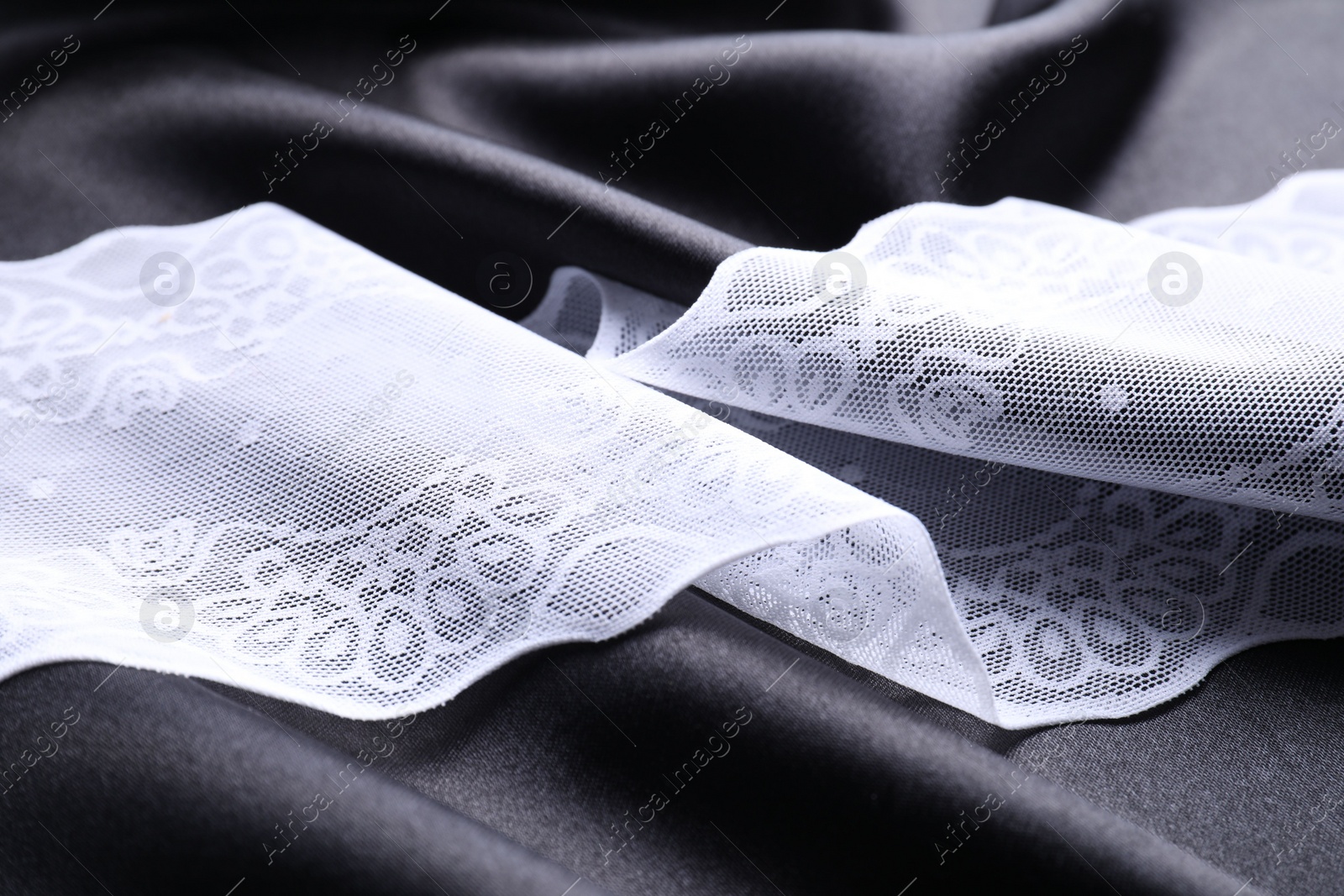 Photo of Beautiful white lace on black fabric, closeup