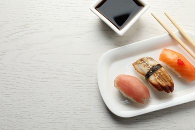Photo of Plate with delicious nigiri sushi and soy sauce on white wooden table, flat lay. Space for text