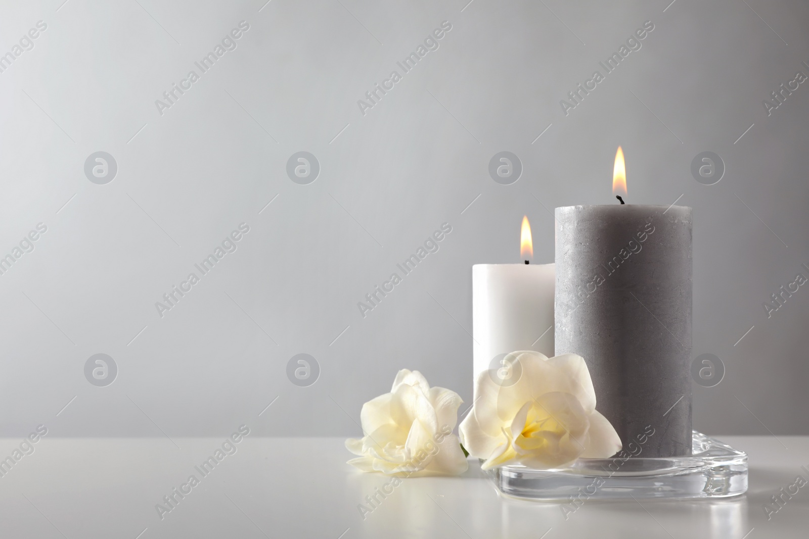 Photo of Wax candles and flowers in glass holder on table against light background. Space for text