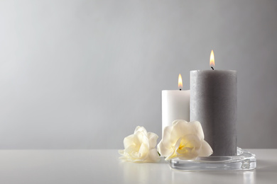 Wax candles and flowers in glass holder on table against light background. Space for text