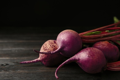 Photo of Fresh beets on dark wooden table against black background. Space for text