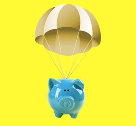 Image of Blue piggy bank with parachute flying on yellow background