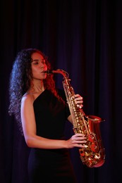 Beautiful African American woman playing saxophone on dark background