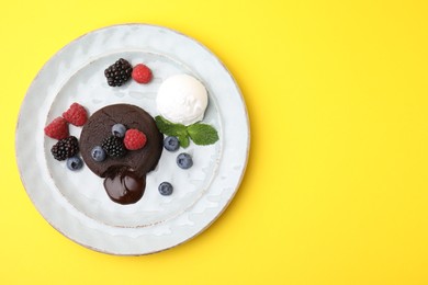 Photo of Delicious chocolate fondant served with fresh berries and ice cream on yellow background, top view. Space for text