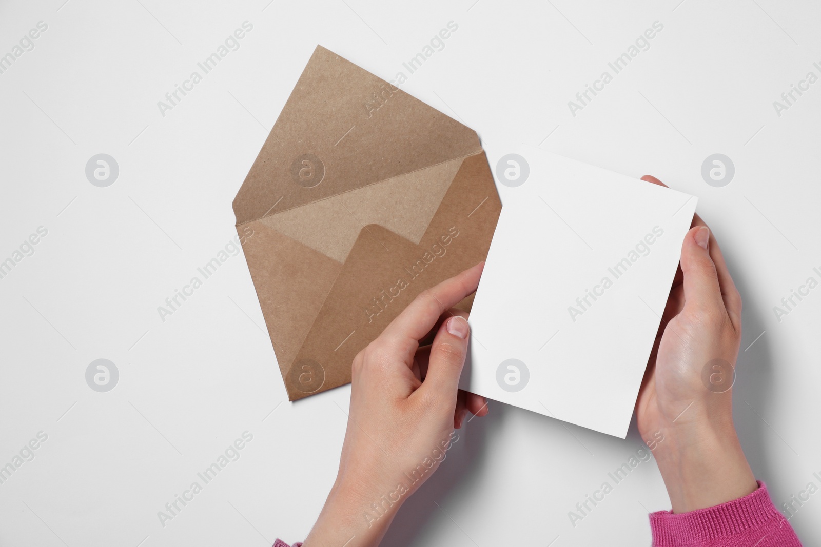 Photo of Woman with blank sheet of paper and letter envelope at white table, top view. Space for text