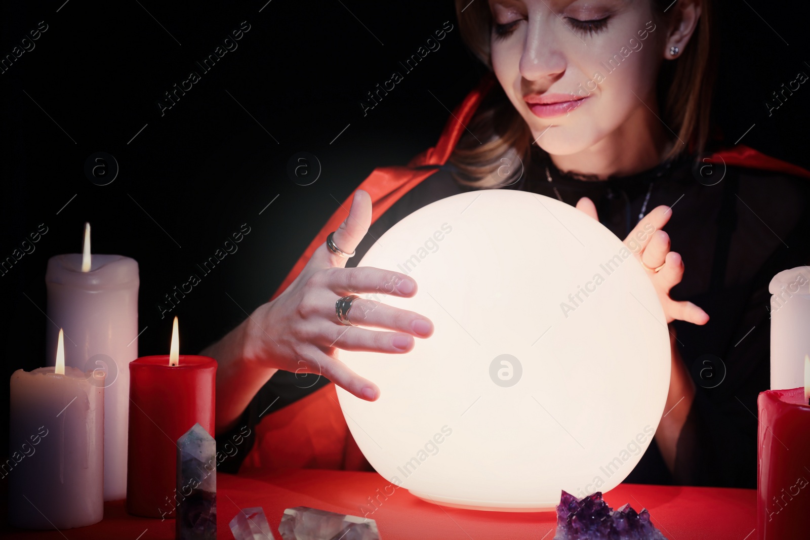 Photo of Soothsayer using glowing crystal ball to predict future at table in darkness. Fortune telling