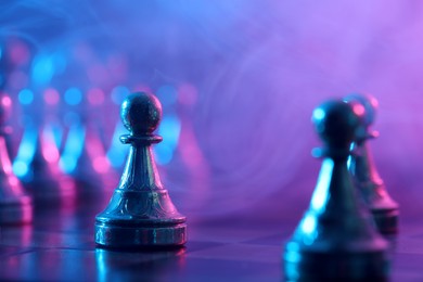 Photo of Chess pawns on checkerboard in color light, selective focus. Space for text
