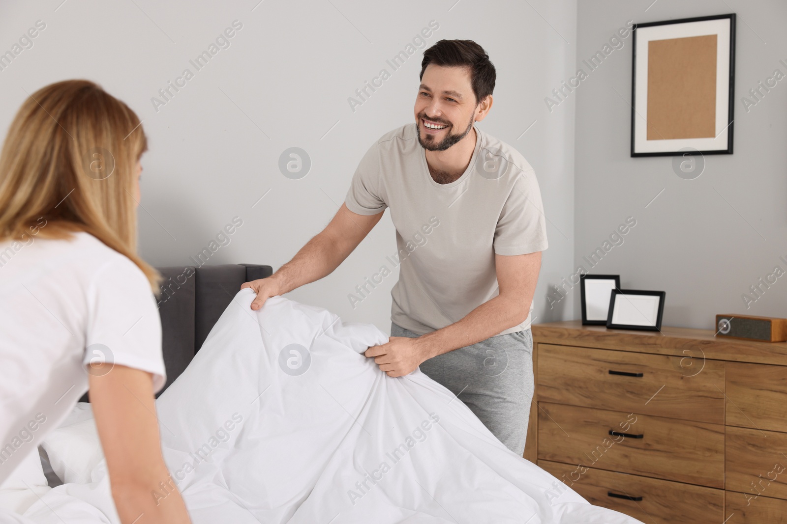 Photo of Couple changing bed linens in room. Domestic chores