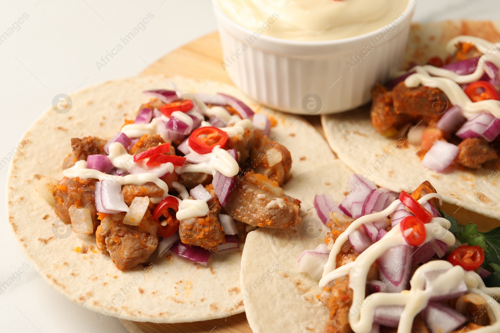 Photo of Delicious tacos with vegetables, meat and sauce on white table, closeup