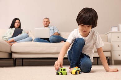 Photo of Child playing with toys and parents working on sofa at home
