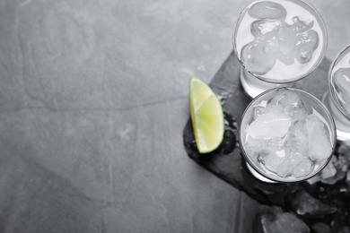 Shot glasses with vodka, ice and lime on grey table, flat lay. Space for text